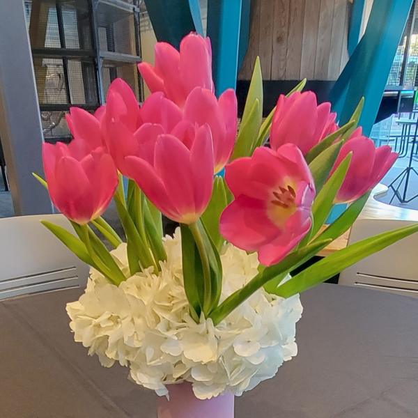 Pink tulips arranged in a pink vase with white flowers at the base