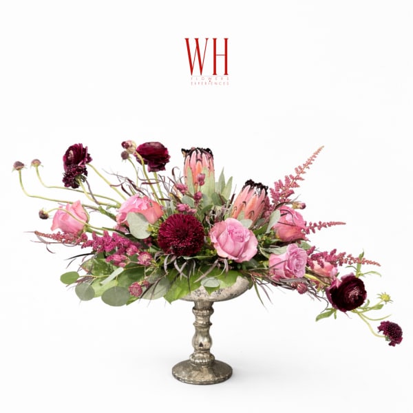 Pink and burgundy floral arrangement in a silver pedestal vase