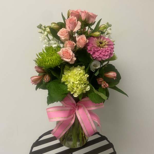Pink roses and mixed blooms in a glass vase with a pink ribbon