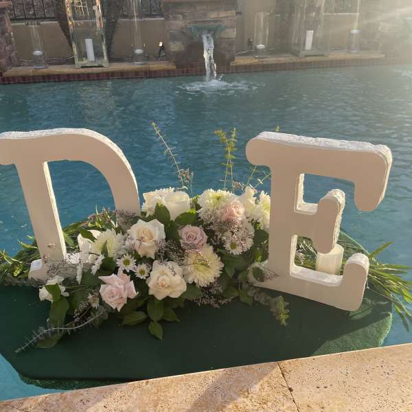 White floral arrangement with large letters spelling "TE" beside a pool