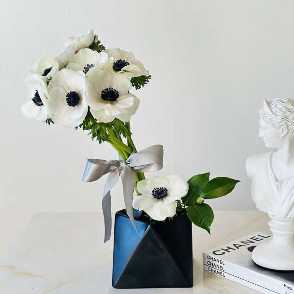 White anemone bouquet in a black vase with a silver ribbon