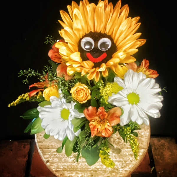 Sunflower-shaped floral arrangement with daisies and orange blooms in a round container