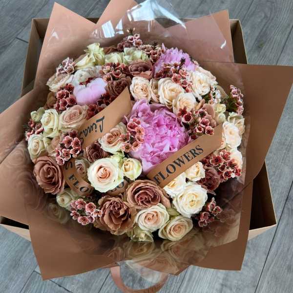 Bouquet of blush and cream roses with pink blooms in brown wrapping