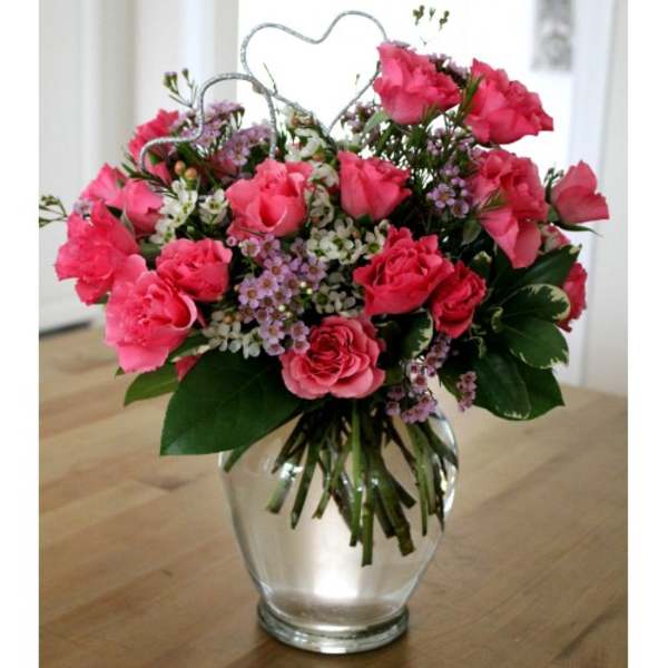 Pink rose bouquet in a clear glass vase with heart picks
