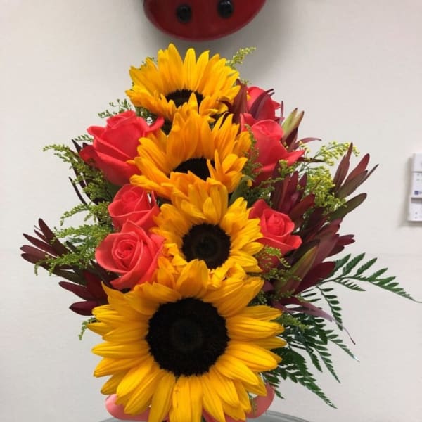 Sunflowers and pink roses in a glass vase with a pink ribbon