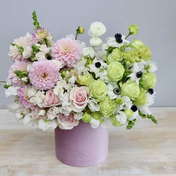 Round pastel arrangement of pink and green flowers in a pink hatbox-style container