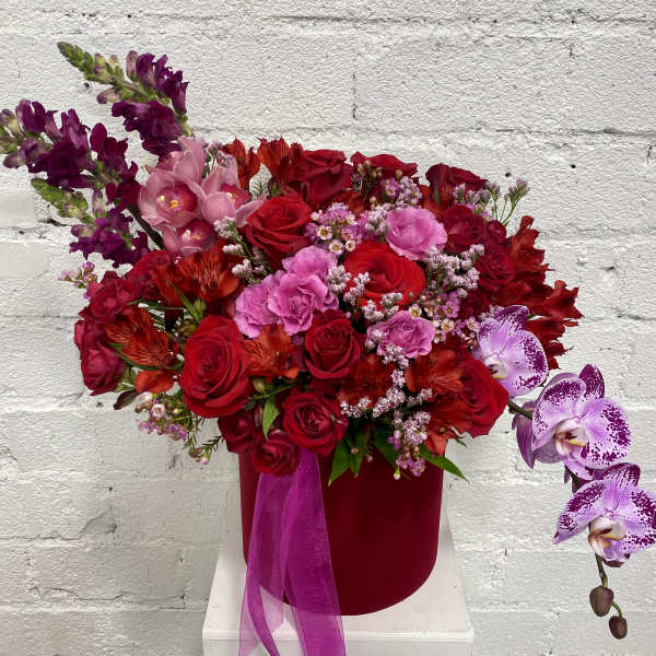 Red and pink floral arrangement in a velvet box with orchid sprays