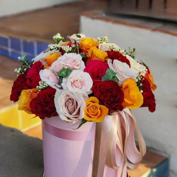 Round bouquet of red, pink, white, and yellow roses in a pink hat box