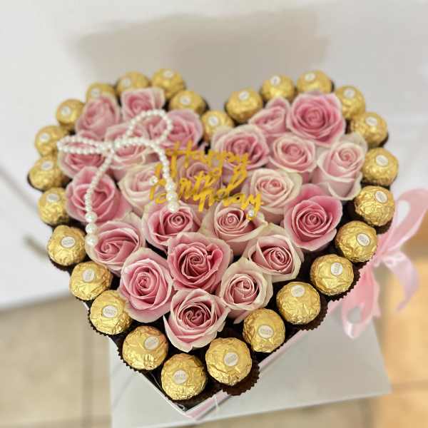 Heart-shaped arrangement of pink roses and gold-wrapped chocolates with a birthday topper