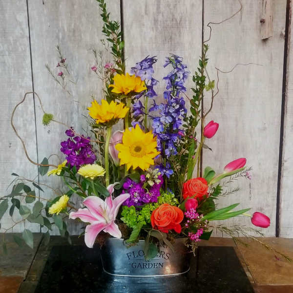 Mixed bouquet in a metal container with sunflowers, lilies, roses, and tulips
