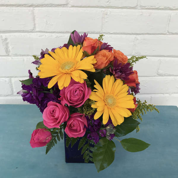 Bright mixed bouquet with yellow daisies, pink roses, and purple flowers in a dark vase