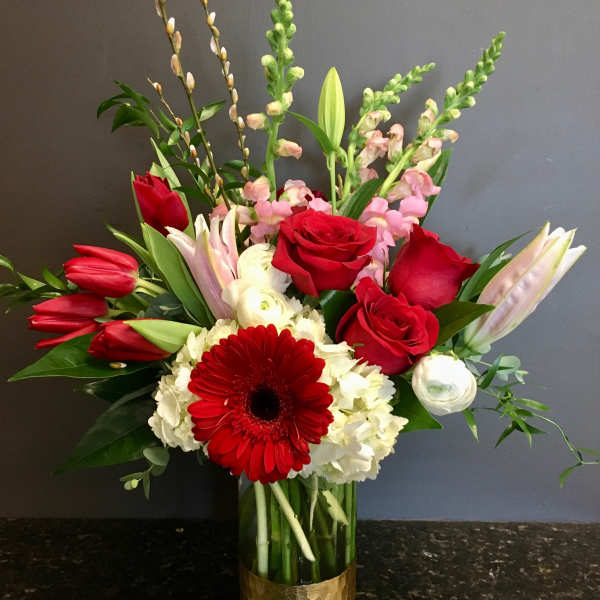 Red roses and lilies arranged in a glass vase with white blooms