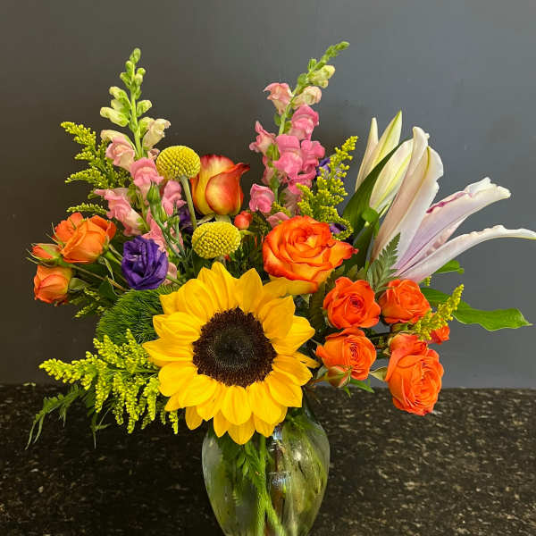 Mixed bouquet with sunflowers, orange roses, and lilies in a glass vase