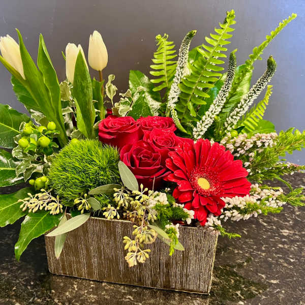 Red roses and a red gerbera daisy in a rectangular vase