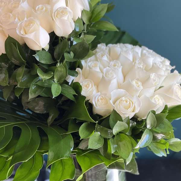 Two bouquets of white roses with green foliage against a blue background
