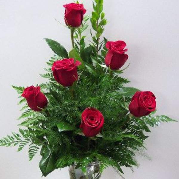 Red roses arranged in a clear glass vase with greenery