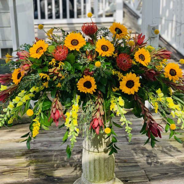 Large floral arrangement with sunflowers and red blooms in a pedestal vase