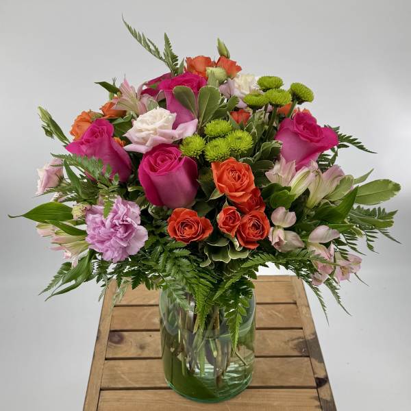 Mixed bouquet of pink, orange, white, and green flowers in a glass vase