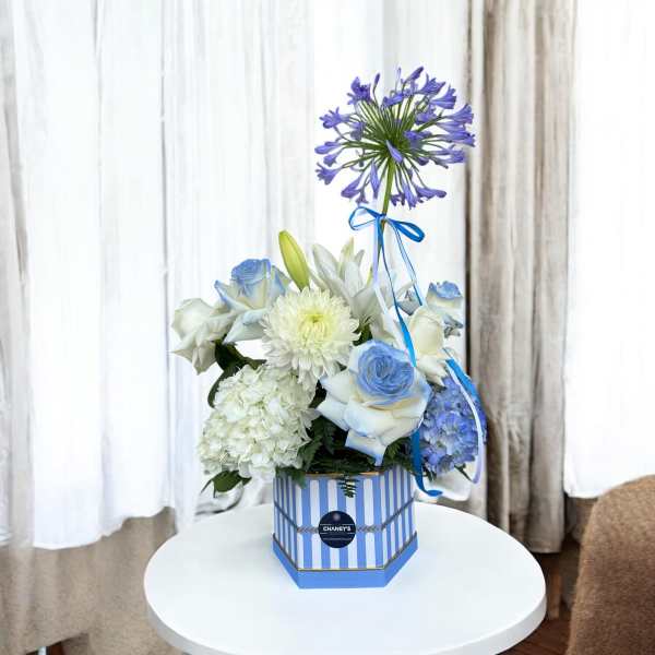 Blue and white floral arrangement in a striped box with a ribbon