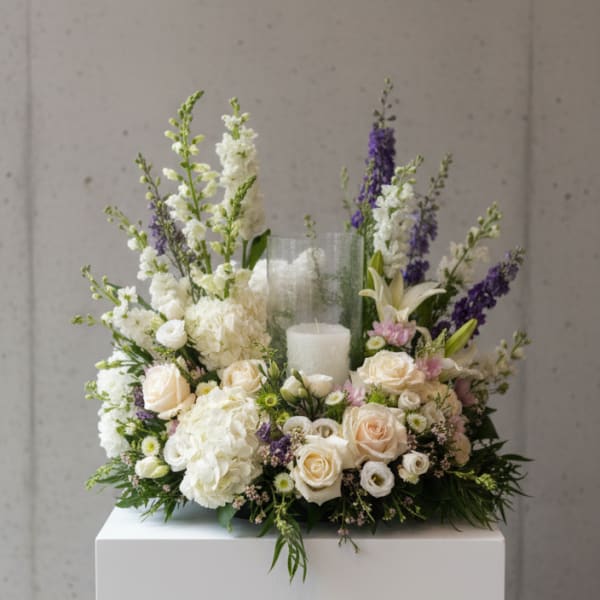 White and cream floral arrangement with purple accents around a candle