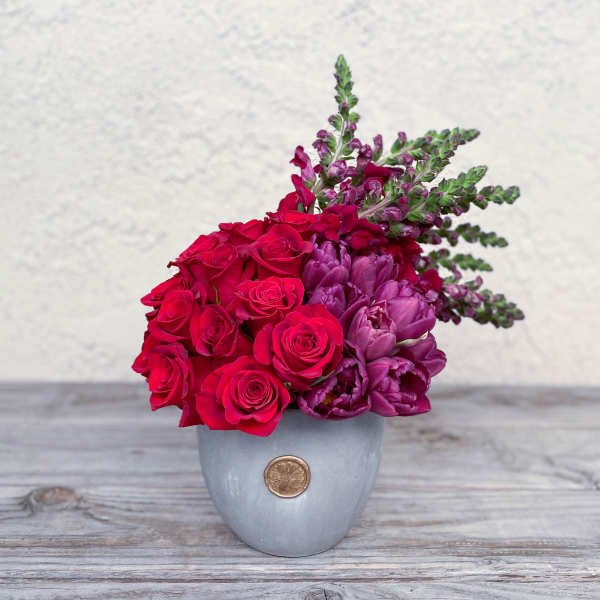 Red roses and purple flowers arranged in a gray vase