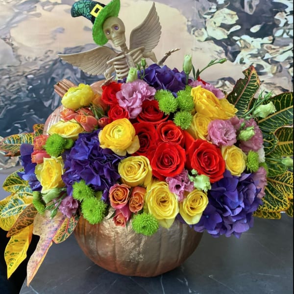 Colorful flower arrangement in a pumpkin container with a skeleton topper