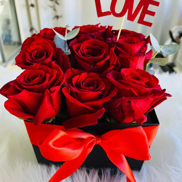 Red roses in a black box with a red ribbon and LOVE topper