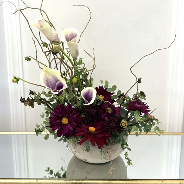 Purple calla lilies and dark dahlias in a white bowl vase