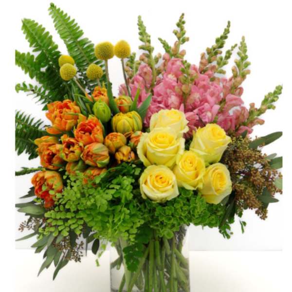 Mixed bouquet of yellow roses, pink snapdragons, and orange tulips in a glass vase