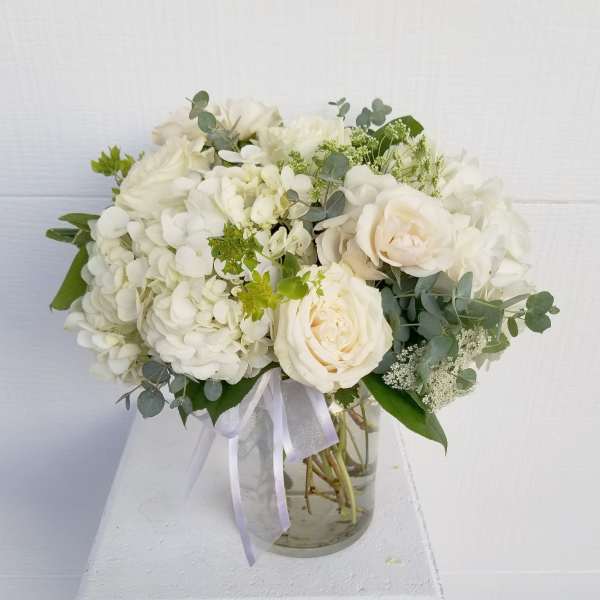 White rose and hydrangea bouquet in a glass vase with ribbon