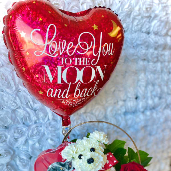 Heart-shaped red balloon above a basket with white flowers and a red rose