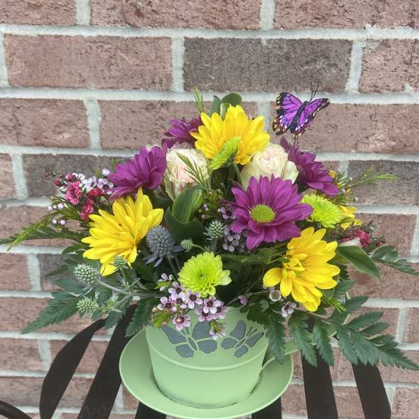 Colorful mixed flower arrangement in a green pot with a butterfly pick