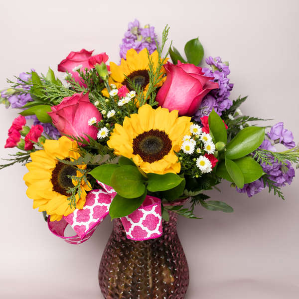 Bouquet of sunflowers, pink roses, and purple flowers in a glass vase