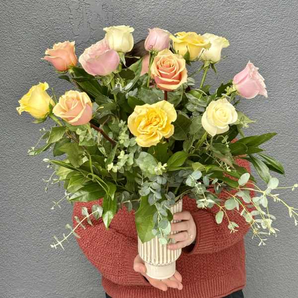Person holding a bouquet of pastel roses in a ribbed vase
