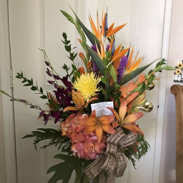 Tropical bouquet with orange bird-of-paradise and mixed blooms in a glass vase