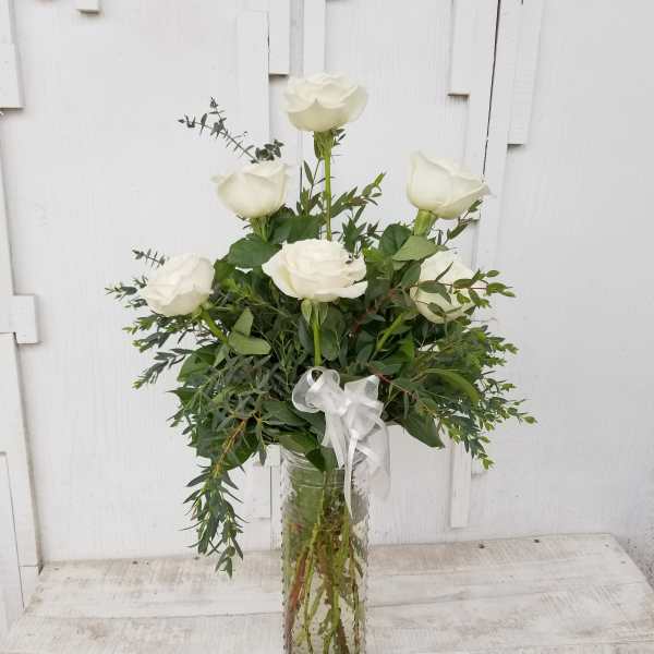 White roses arranged in a clear glass vase with a white ribbon