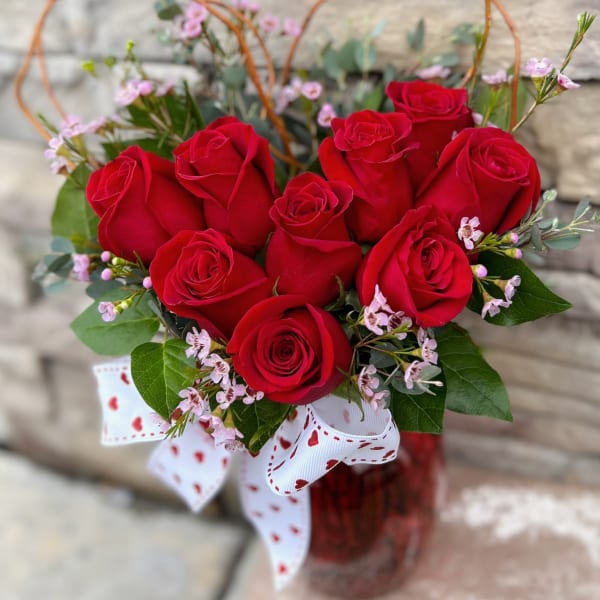 Red roses arranged in a glass vase with a heart-patterned ribbon