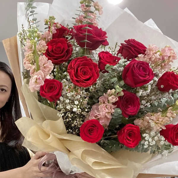 Large bouquet of red roses and pale pink flowers wrapped in white and beige paper