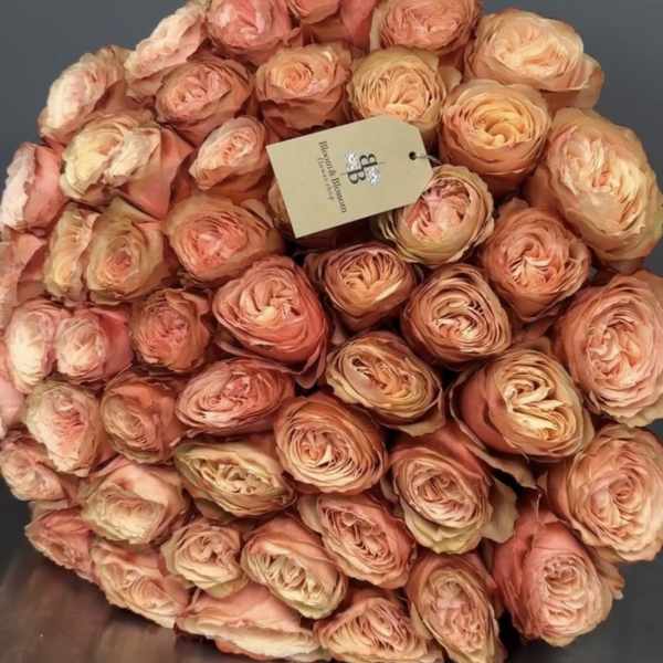 Round bouquet of peach ranunculus flowers with a tag