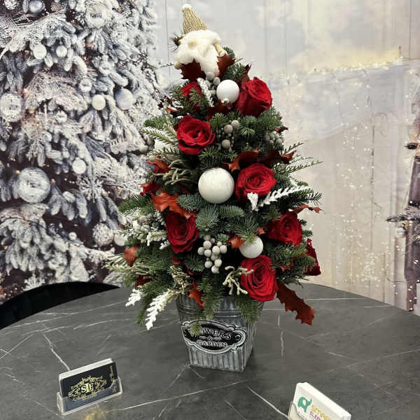 Small Christmas tree arrangement with red roses and white ornaments in a metal container