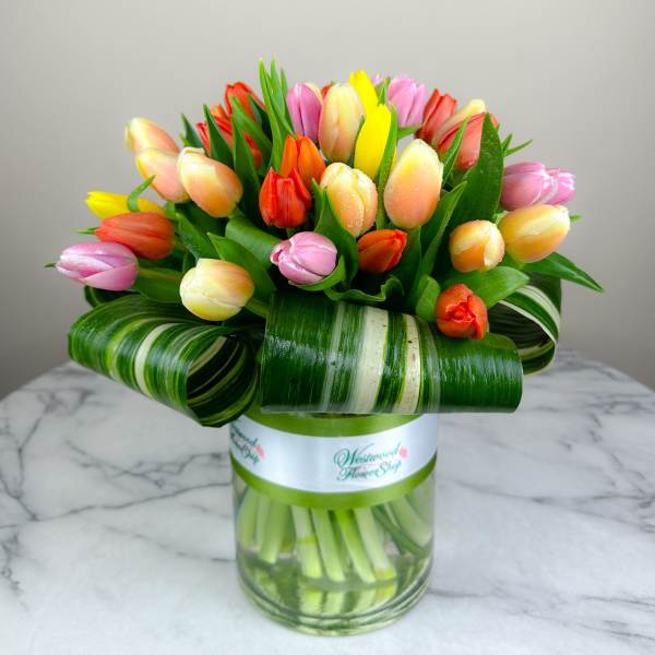 Colorful tulip bouquet in a glass vase with striped leaf wrap