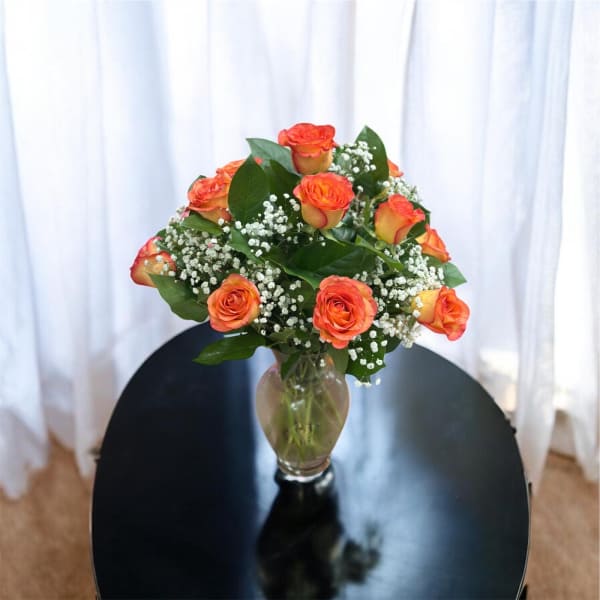 Bouquet of bright orange roses with white filler flowers in a clear glass vase on a black table