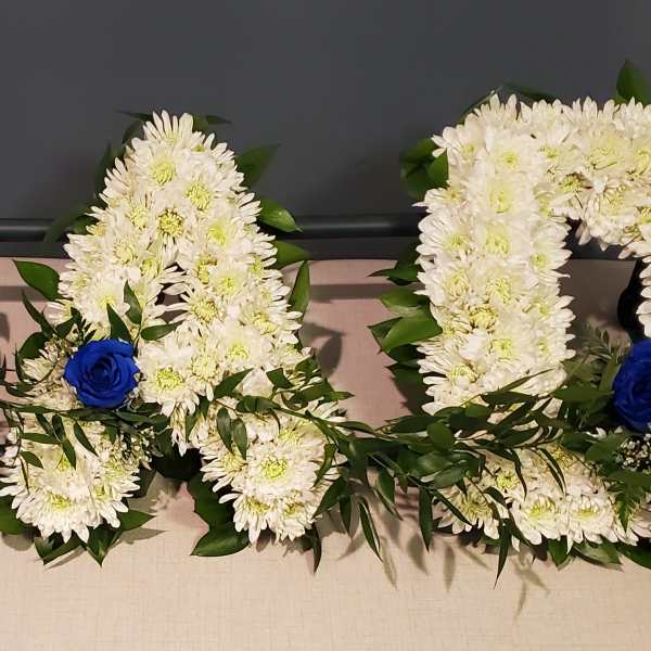 Three floral letters made of white flowers with blue roses and greenery accents.