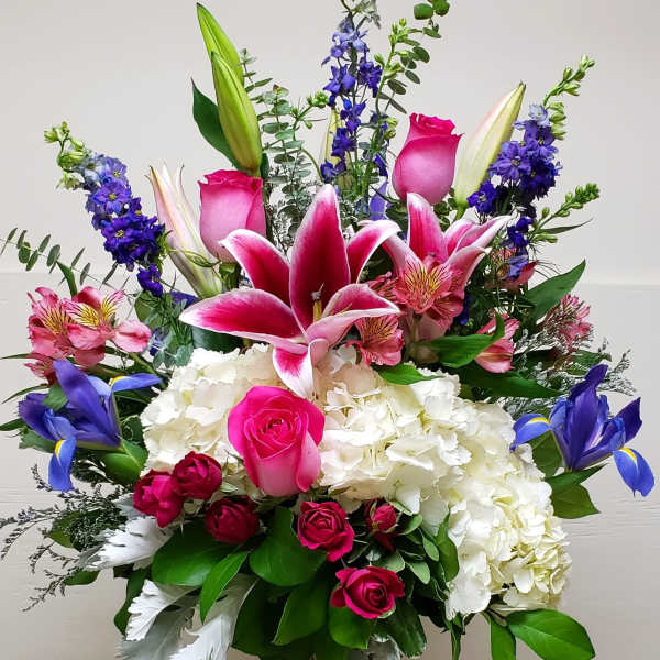 Tall mixed bouquet with pink lilies, roses, hydrangea, and blue iris in a glass vase