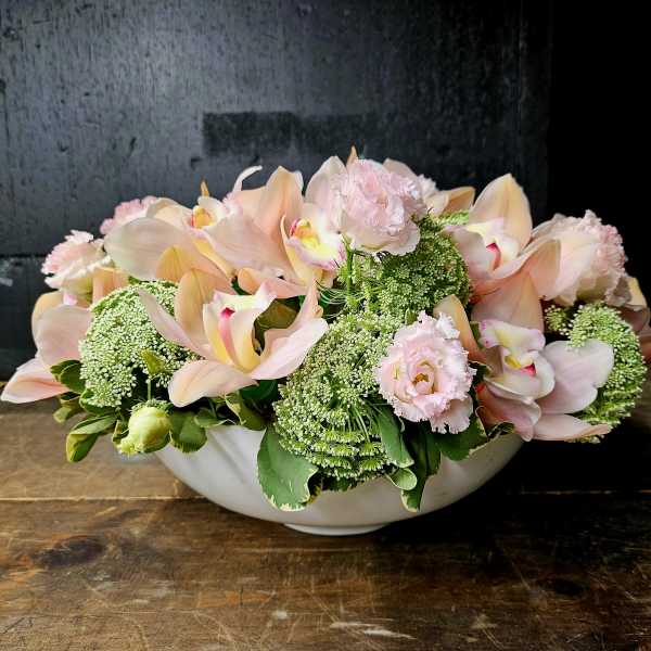 Low floral arrangement of pale pink orchids and ruffled pink blooms in a white bowl