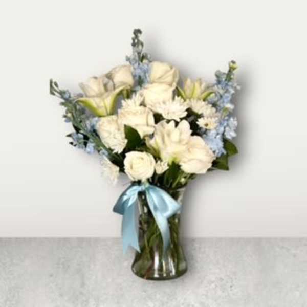White flowers and pale blue blooms in a glass vase with a blue ribbon