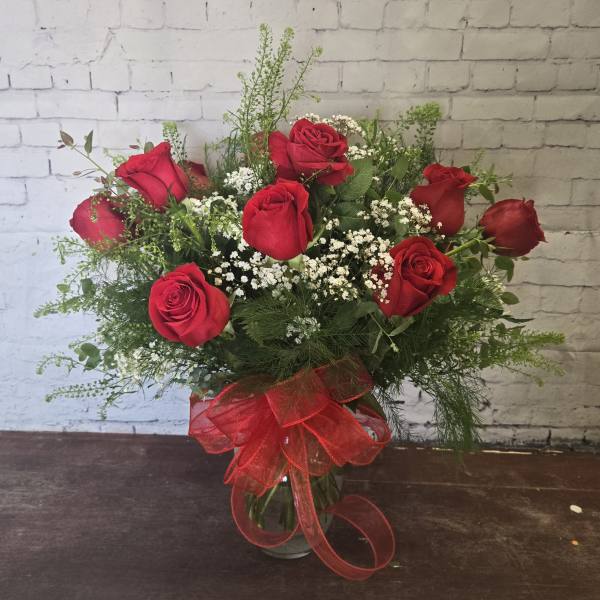 Red roses arranged in a glass vase with baby's breath and a red ribbon