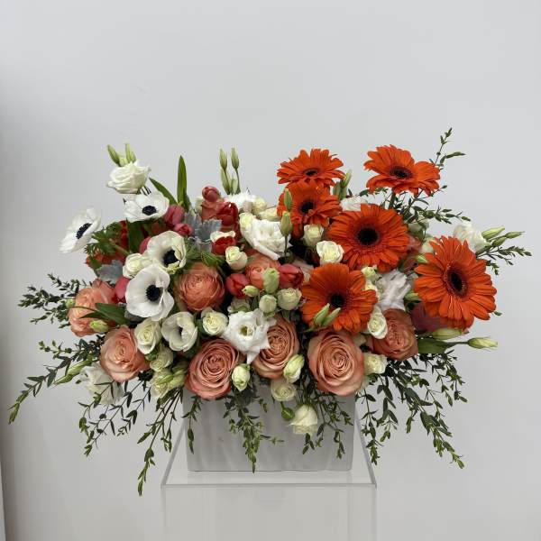 Large bouquet of orange gerbera daisies and peach roses in a white container