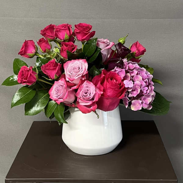 Pink and red roses with purple hydrangea in a white vase