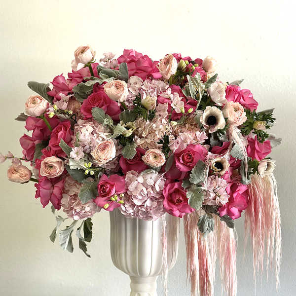 Pink floral arrangement in a white pedestal vase